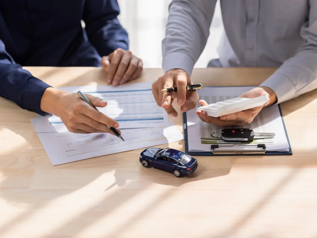dealer salesman giving car key to owner client signing insurance document or rental car lease