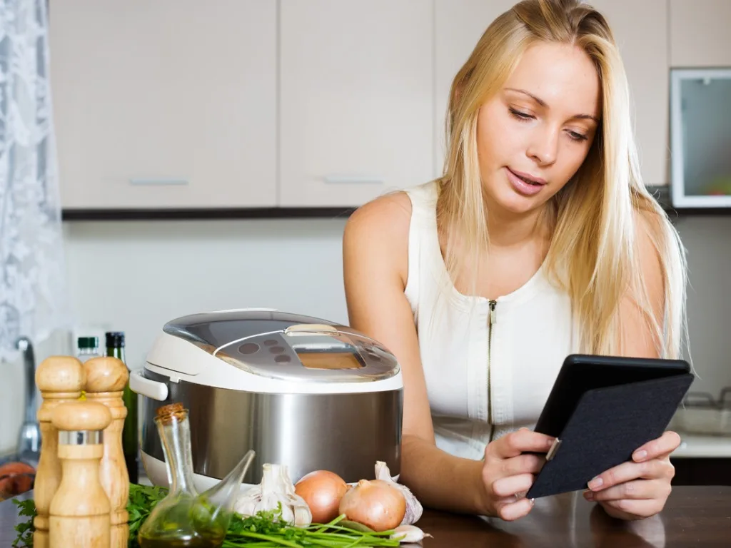 woman reading ereader and cooking with crockpot